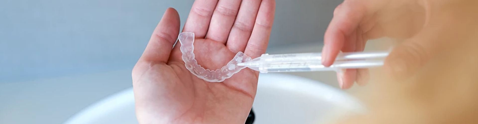 hands injecting whitening gel into clear tray